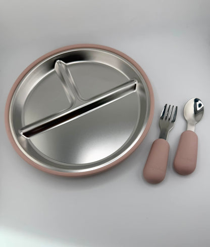 A stainless steel divided baby plate with a dusty pink silicone rim, accompanied by a matching fork and spoon with pink handles, on a light gray background.